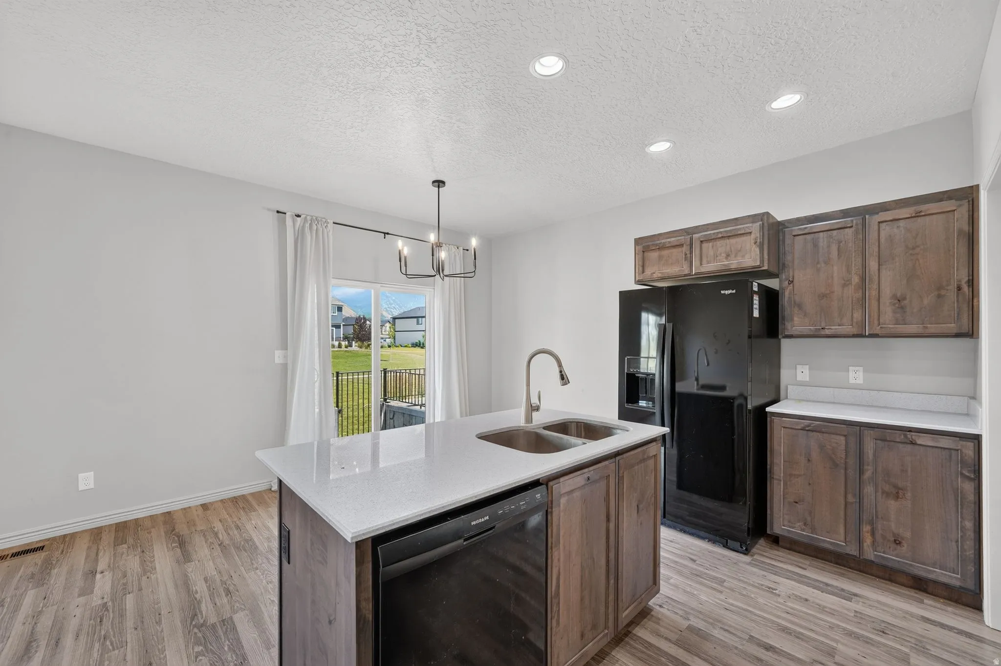 Kitchen featuring a center island with a double basin sink and a black dishwasher, wood-finish flooring, recessed lighting, and a sliding glass door providing access to the backyard