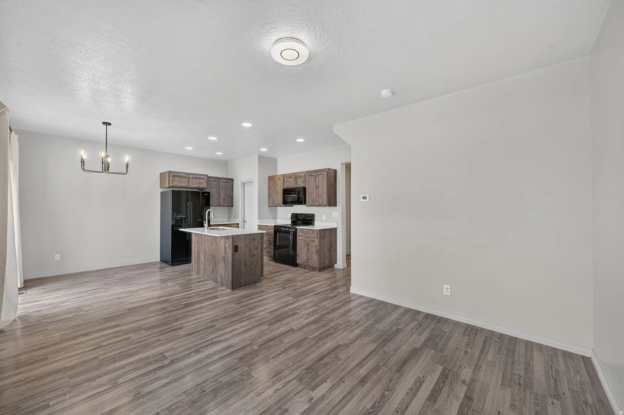 Open-concept living area featuring wood-finish flooring, recessed lighting, and a modern chandelier
