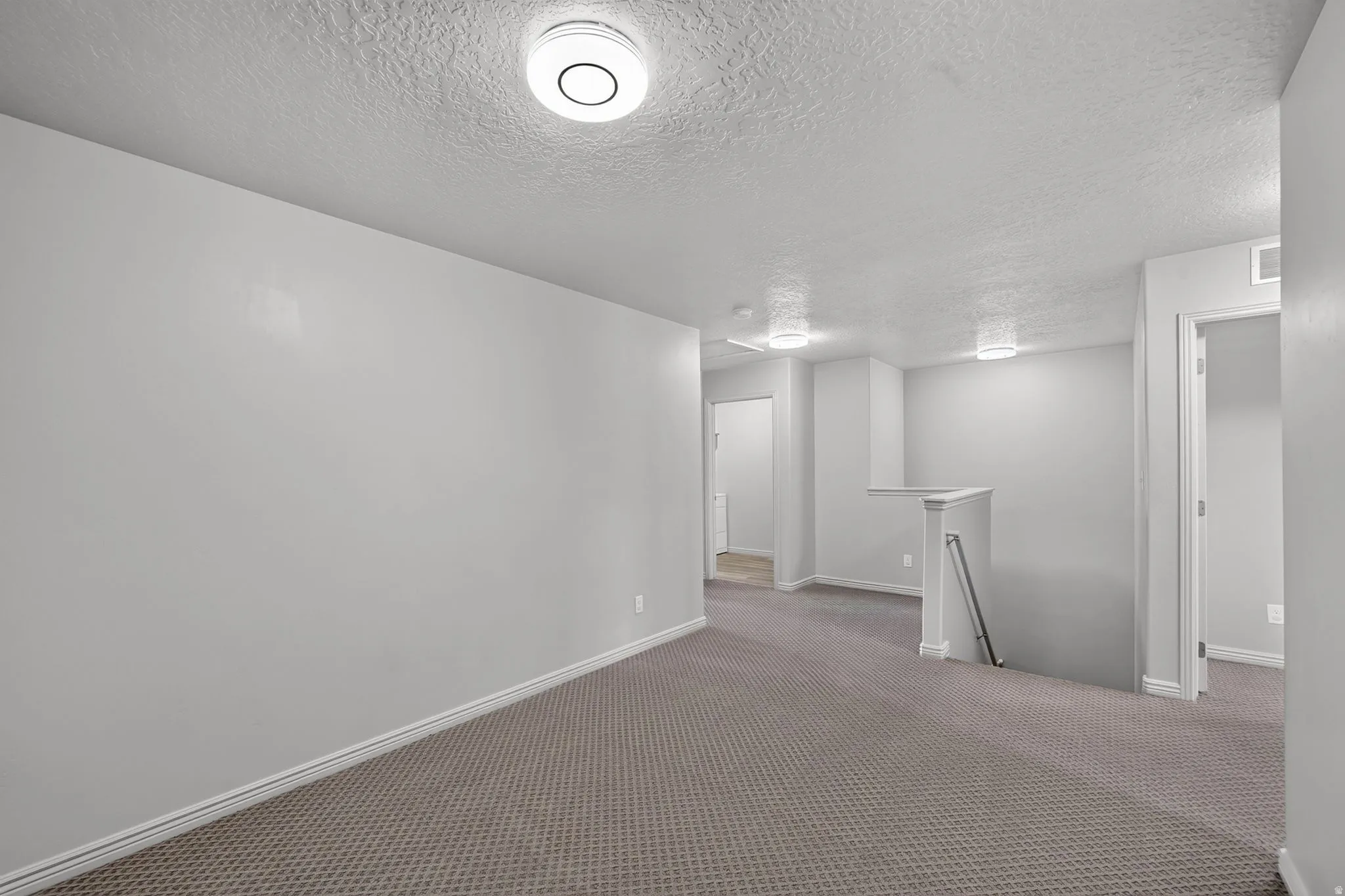 Spacious carpeted room featuring light gray walls, white baseboards, and multiple flush-mount ceiling lights