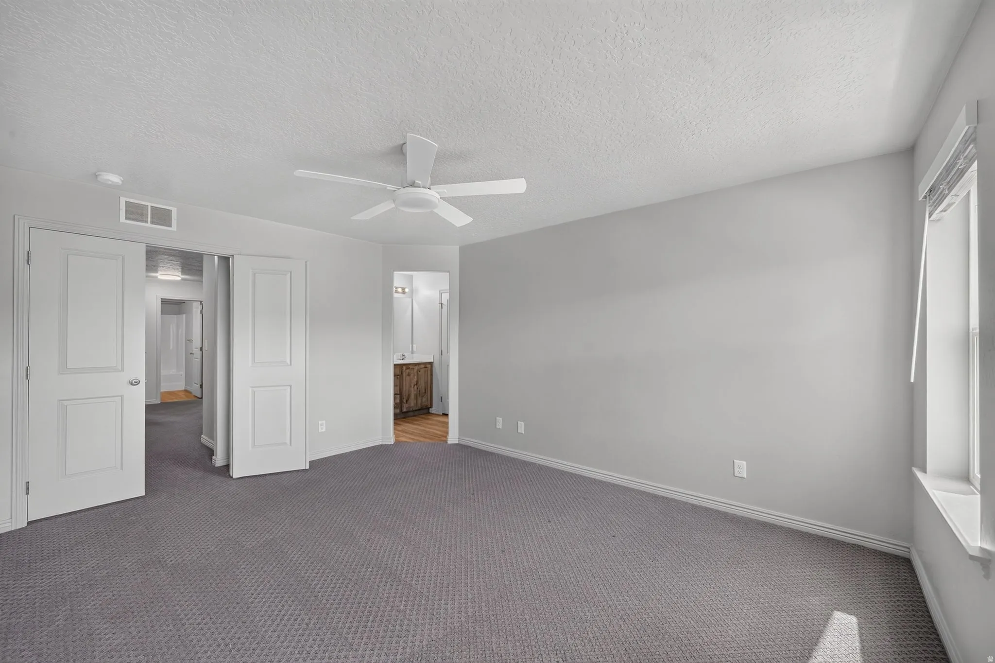 Spacious room featuring gray carpet flooring, white walls, a ceiling fan, and a window with blinds