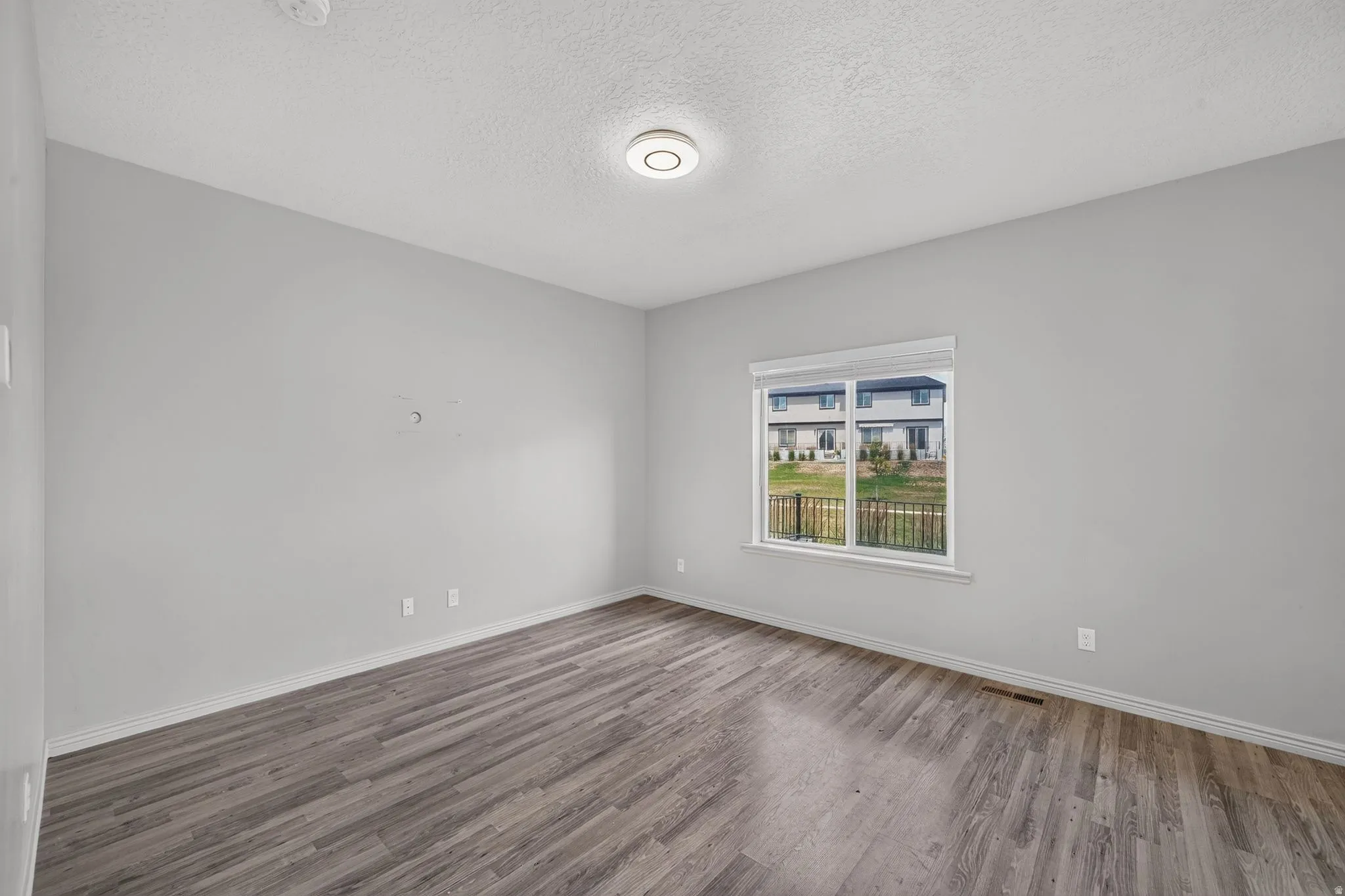 Spacious room featuring wood-finish flooring, light grey wall paint, white baseboards, and a large window with white blinds