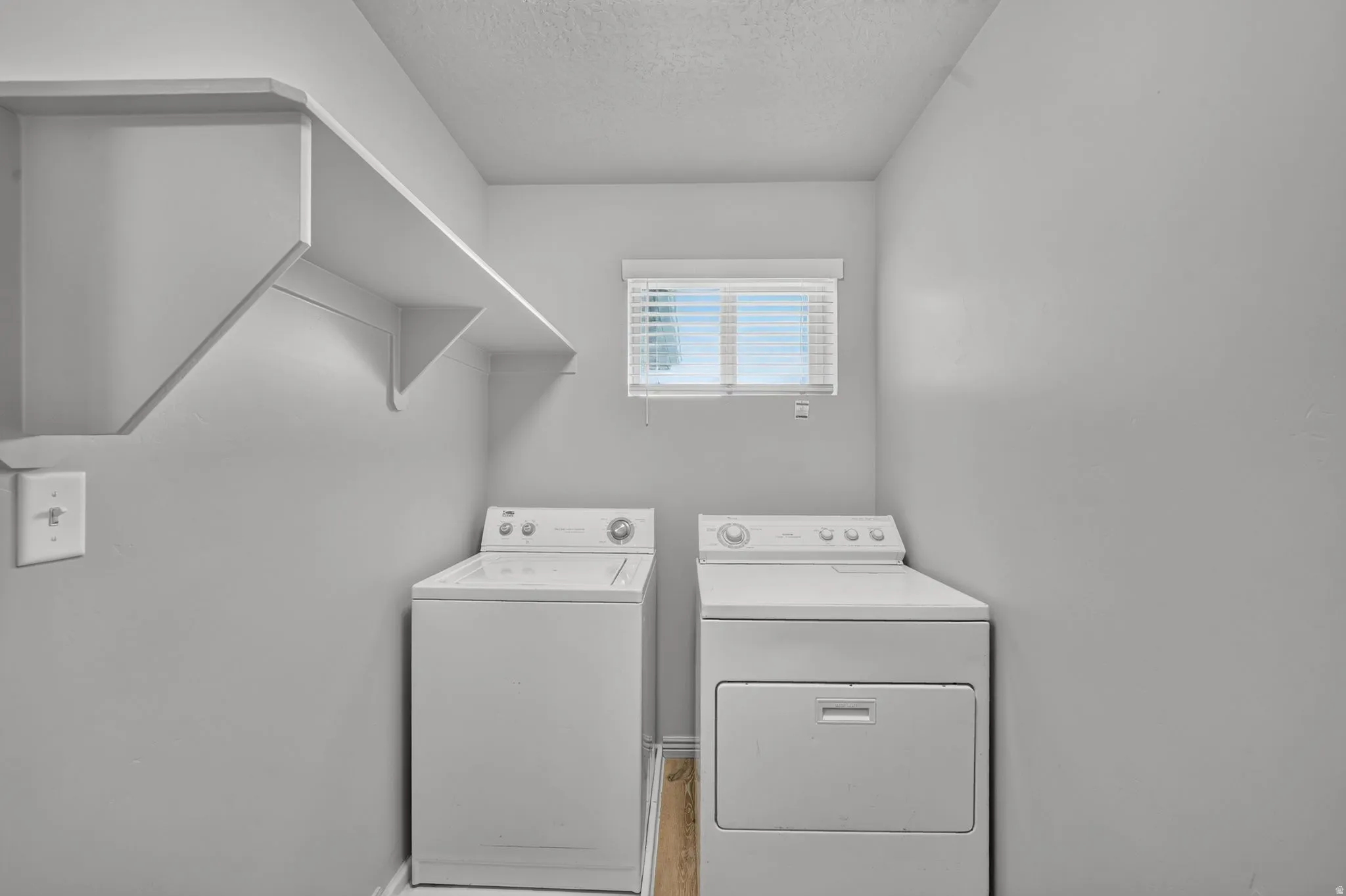 Dedicated laundry area featuring built-in shelving, a window with horizontal blinds, and wood-finish flooring
