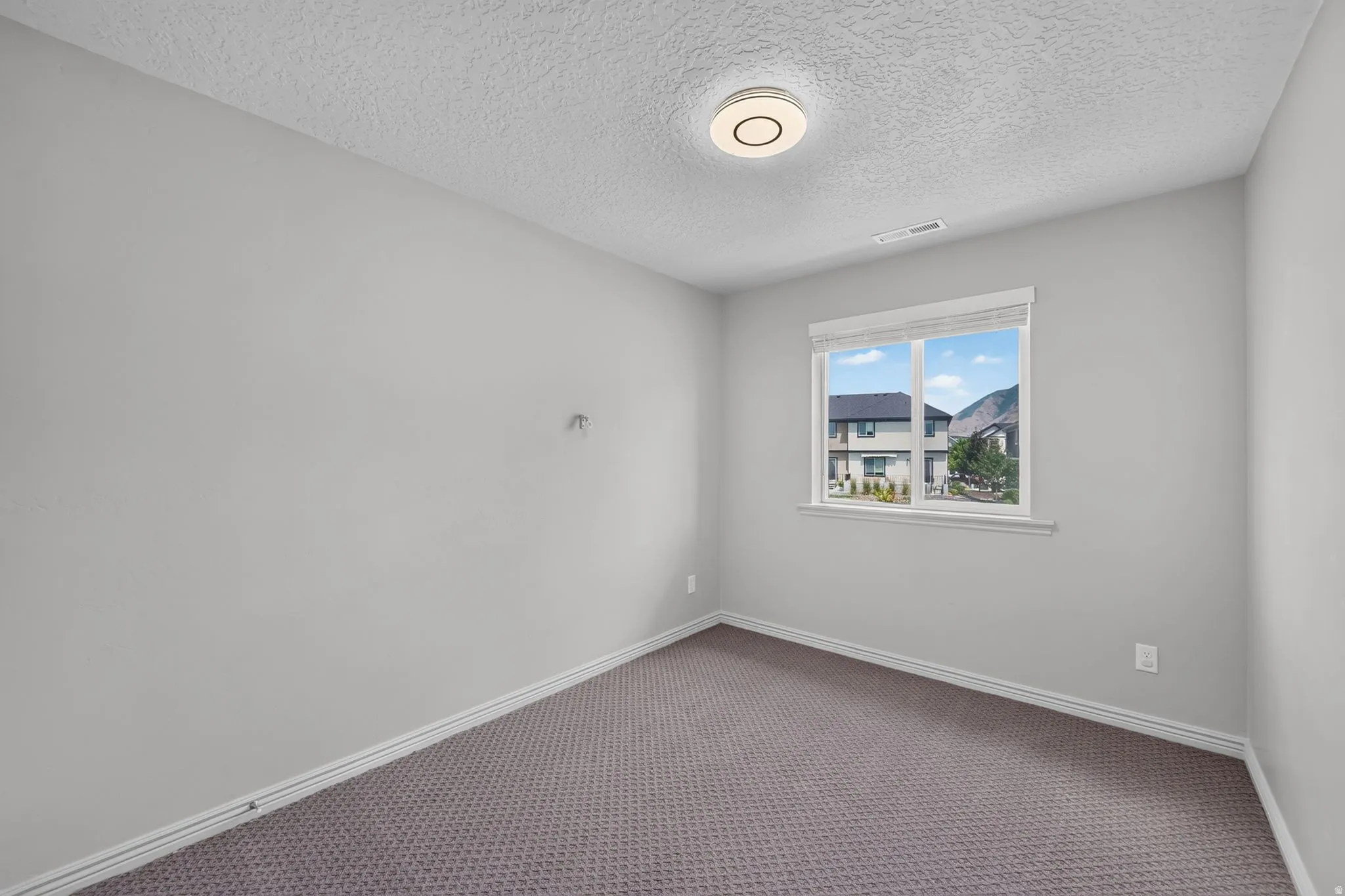 Light-filled room featuring a single window, neutral wall paint, textured ceiling, and gray patterned carpeting