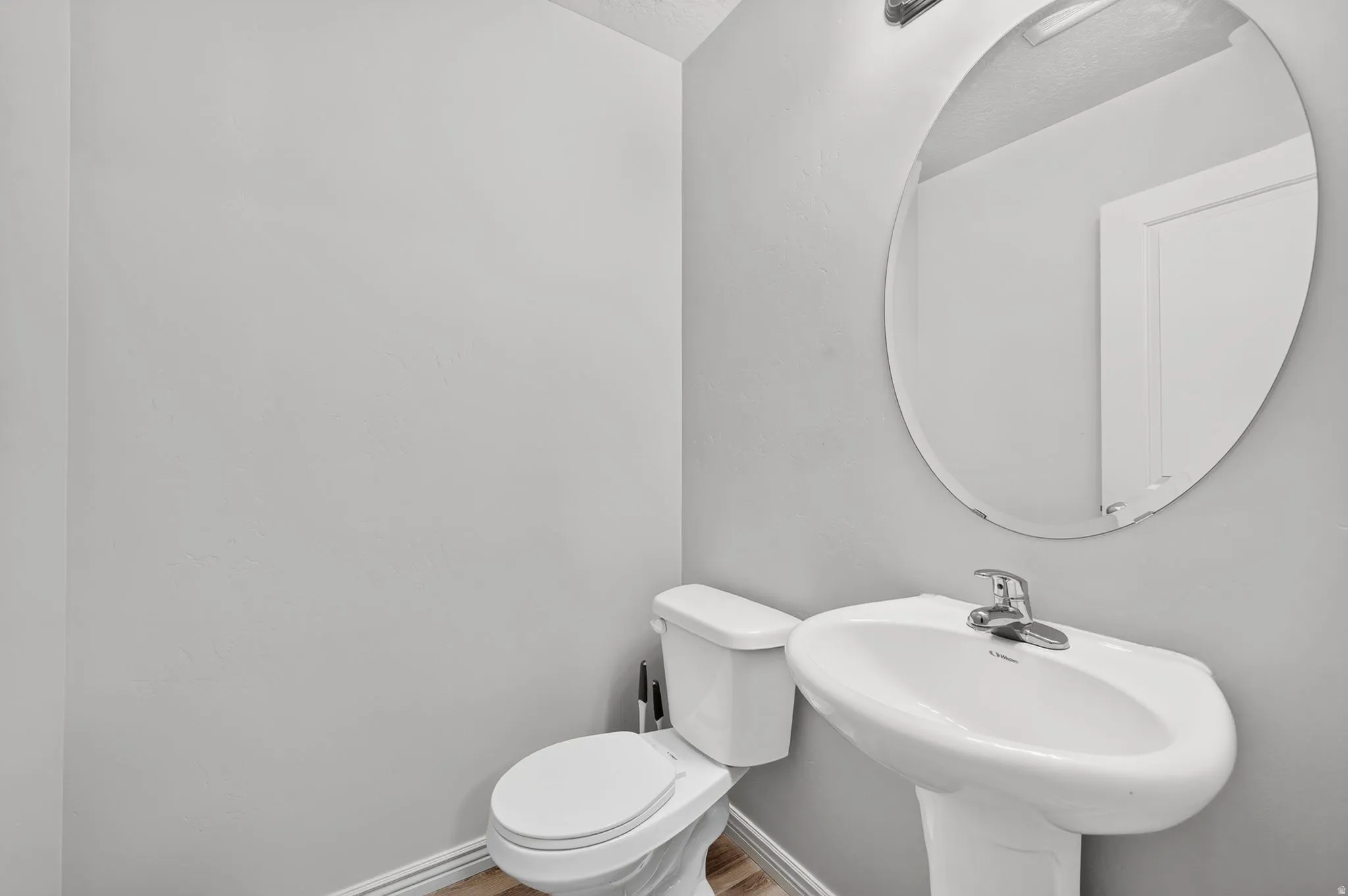 Pedestal sink with chrome faucet, oval frameless mirror, and recessed lighting