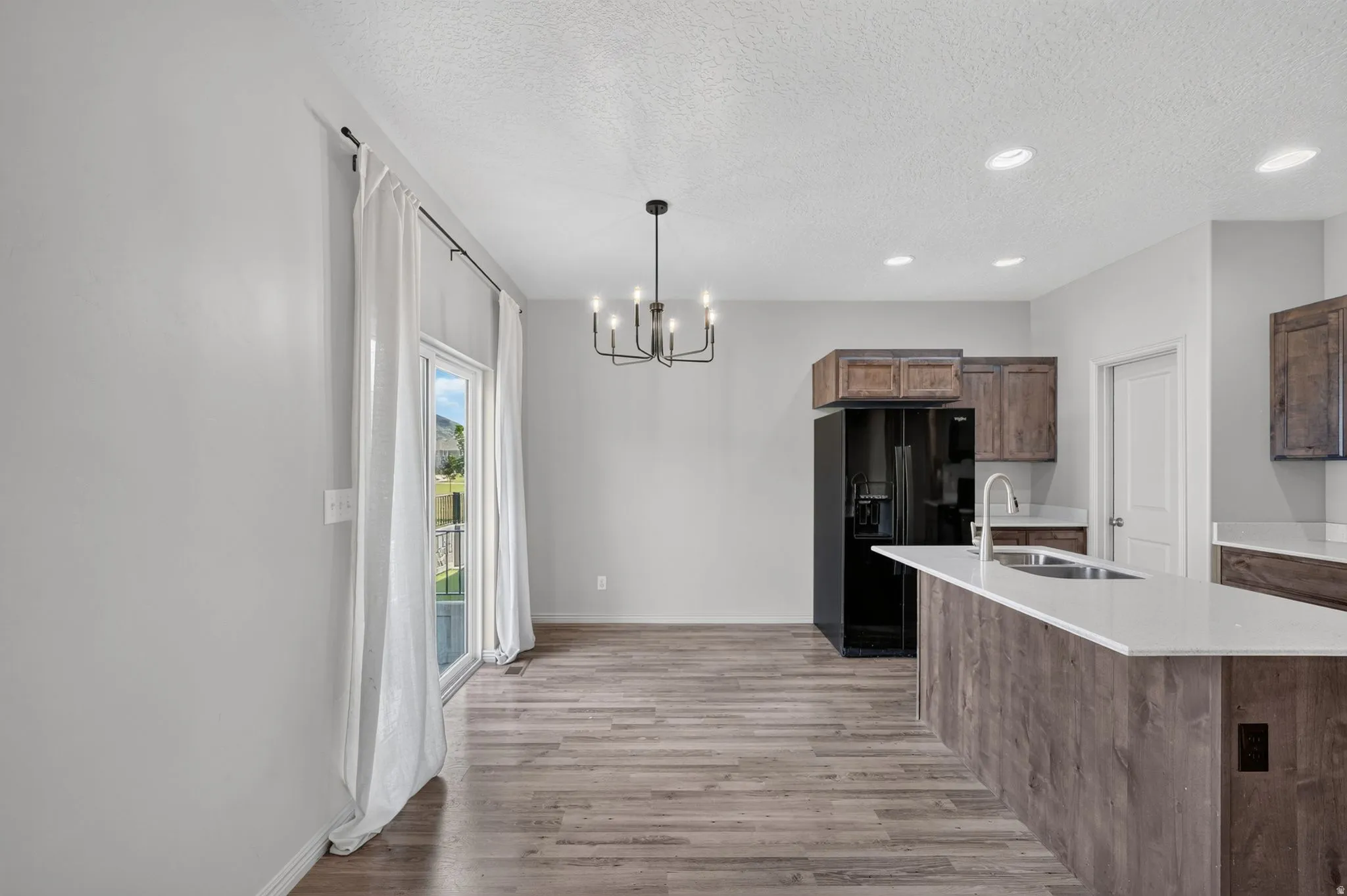 Open-concept kitchen and dining area featuring wood-finish flooring, a kitchen island with a white countertop, dark wood-finish cabinetry, and a black appliance package