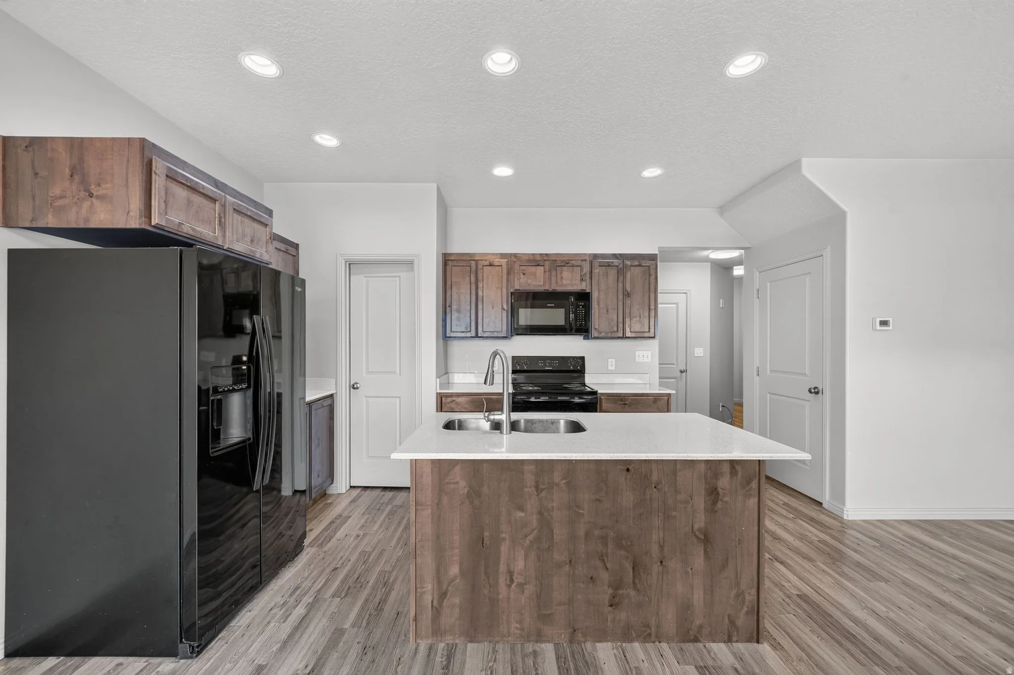 Modern kitchen featuring a central island with a solid surface countertop and undermount double sink