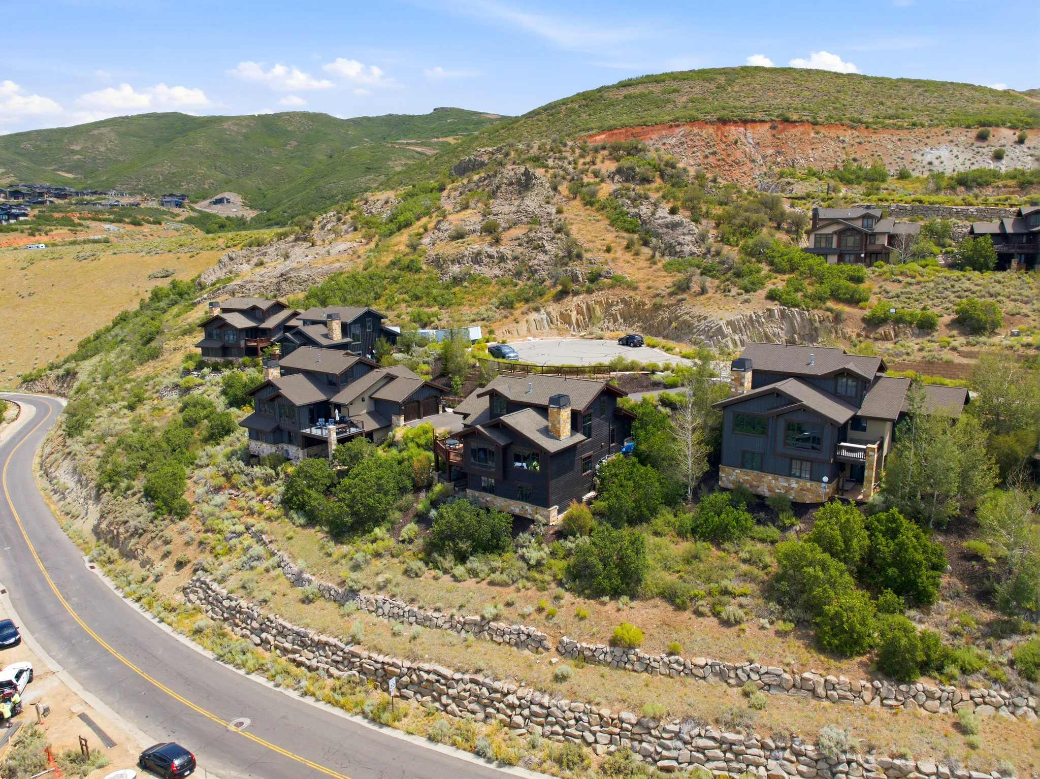 Hillside community featuring multiple residences with dark-toned exteriors, stone accents, and varied rooflines