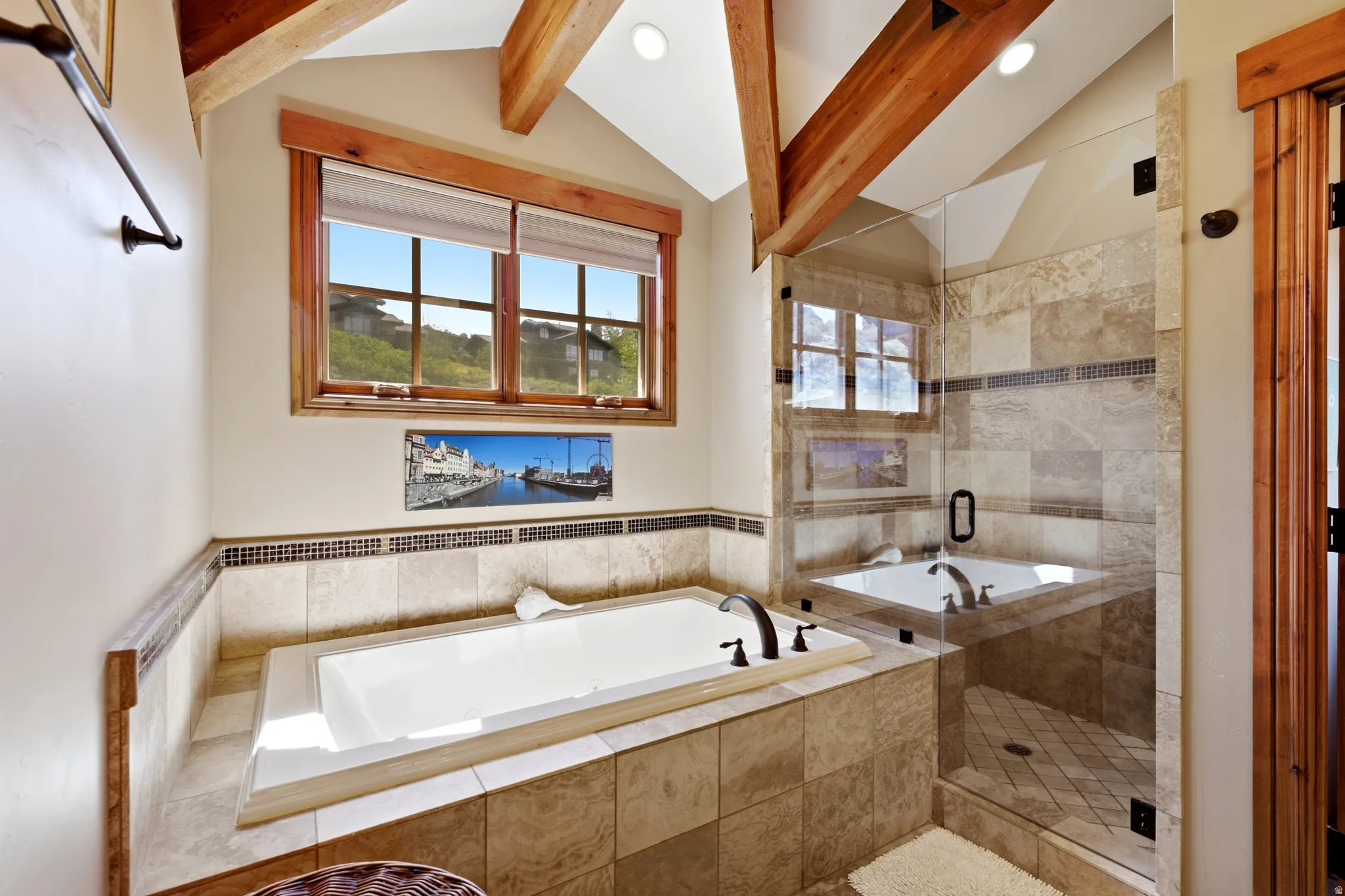 Spacious bathroom featuring a built-in soaking tub, a frameless glass shower enclosure, and a vaulted ceiling with exposed wood beams