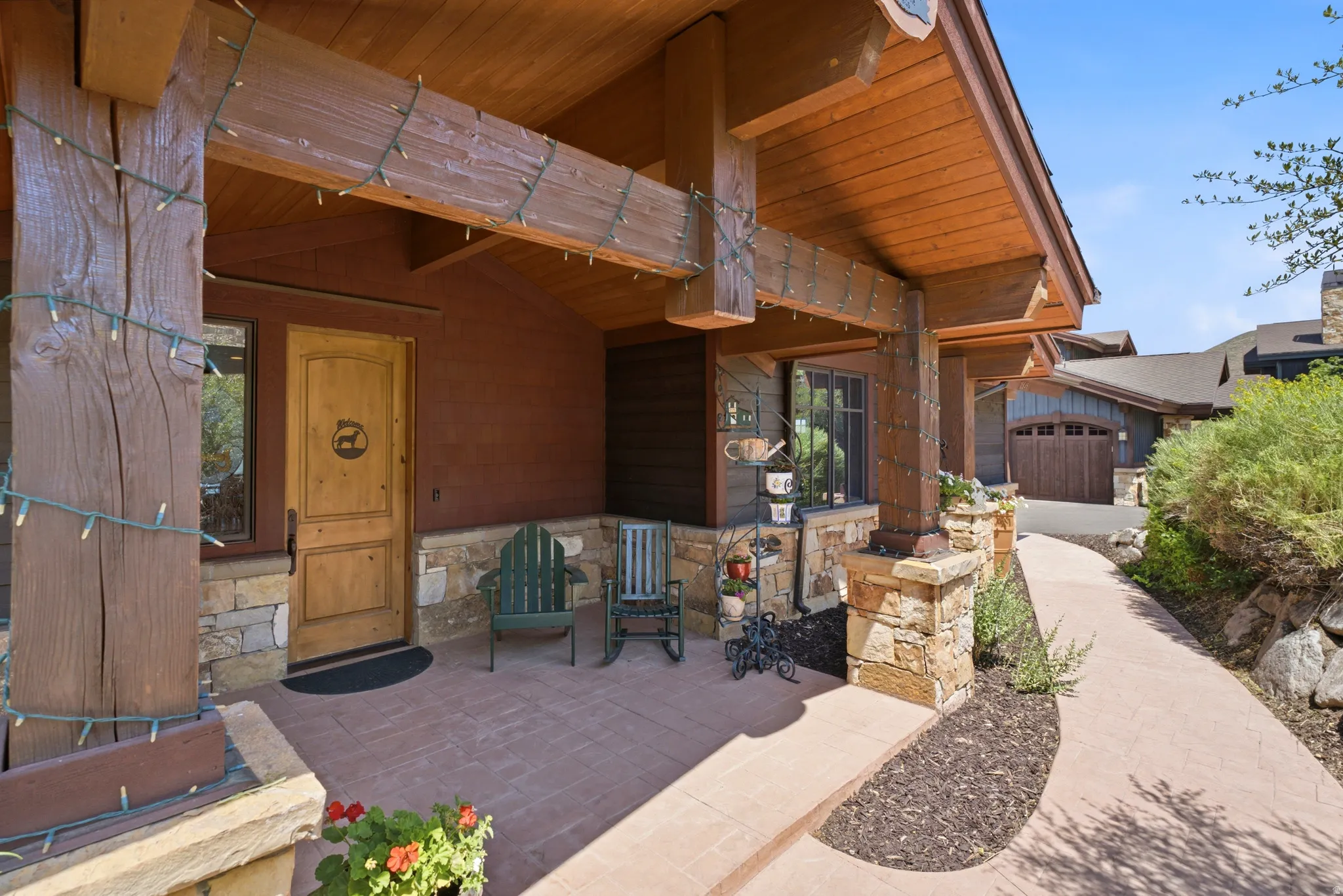 Covered entry with stone accents, exposed wood beams, a natural wood entry door, and a paved walkway