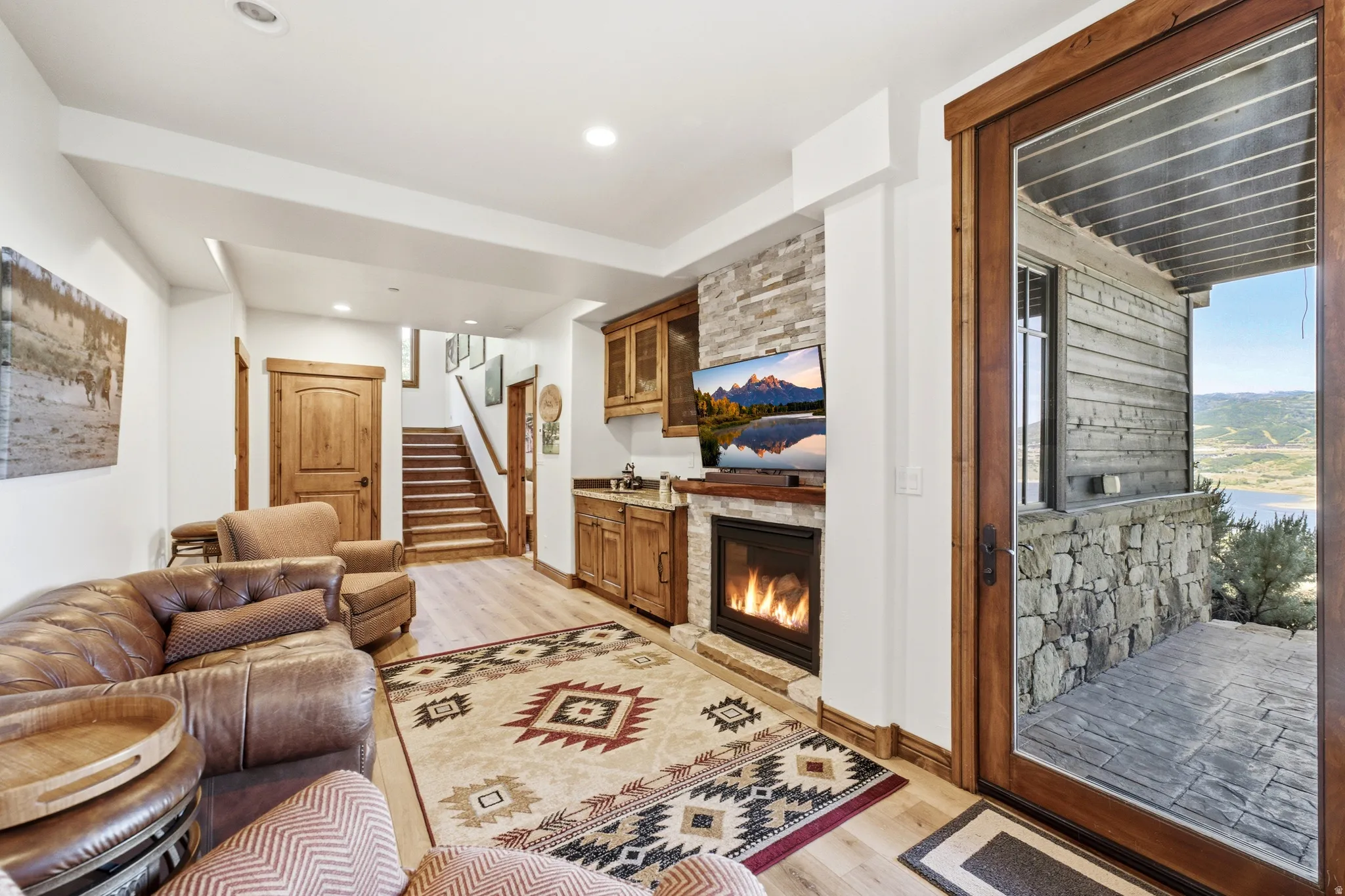 Living area featuring a stone accent wall with a built-in fireplace, wood-finish flooring, recessed lighting, and a wet bar with wood cabinetry and a countertop