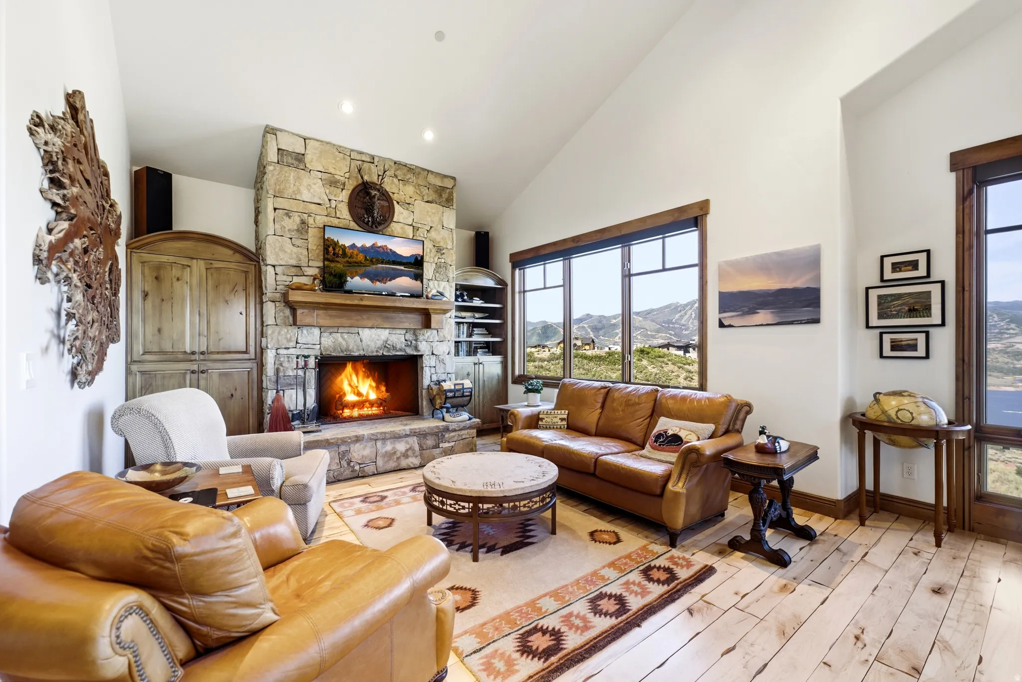 Living area featuring a floor-to-ceiling stone fireplace with a wood mantle, vaulted ceilings, and wide plank wood flooring
