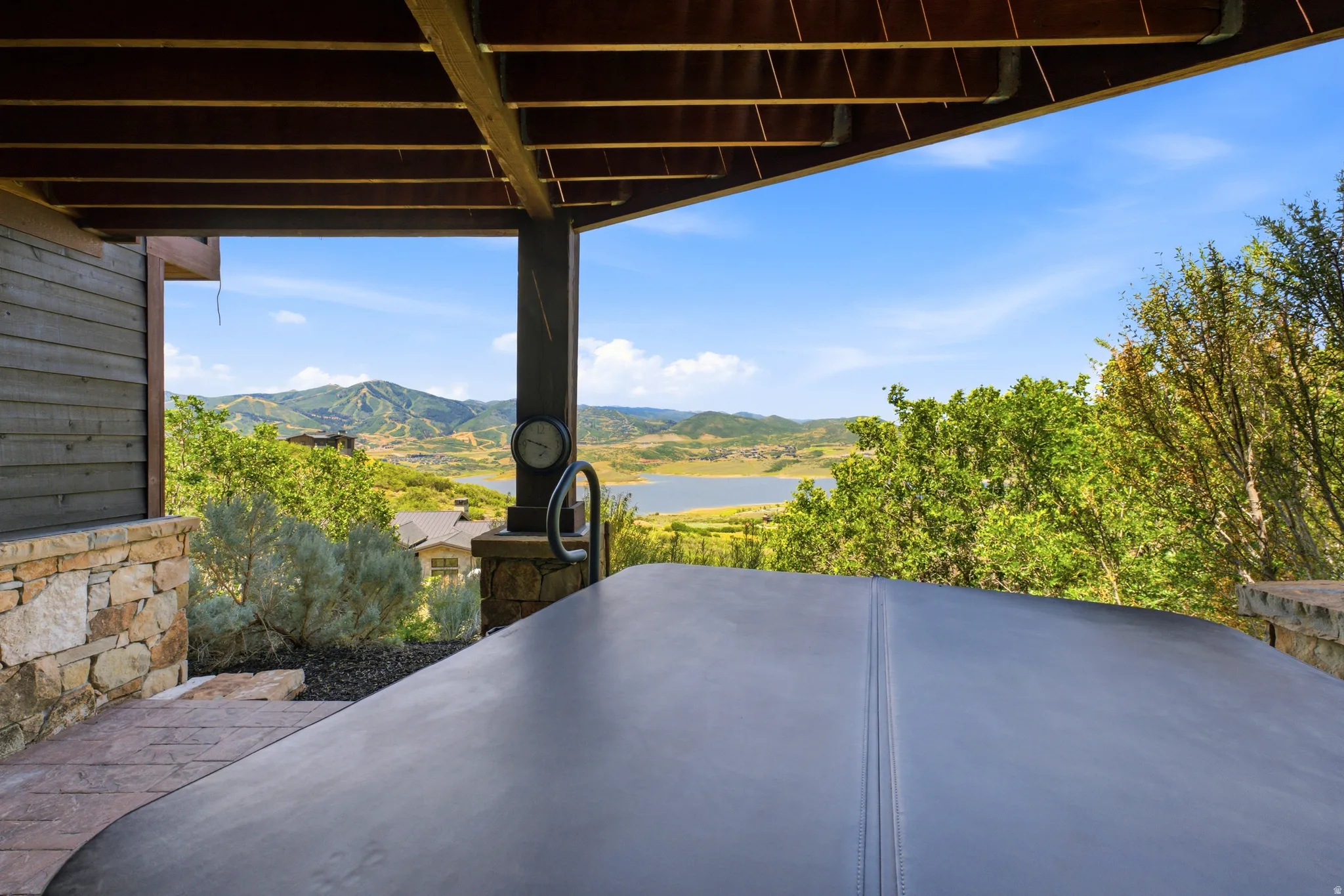 Covered outdoor patio with a spa, stone facade, wood plank siding, and open mountain and lake scenery