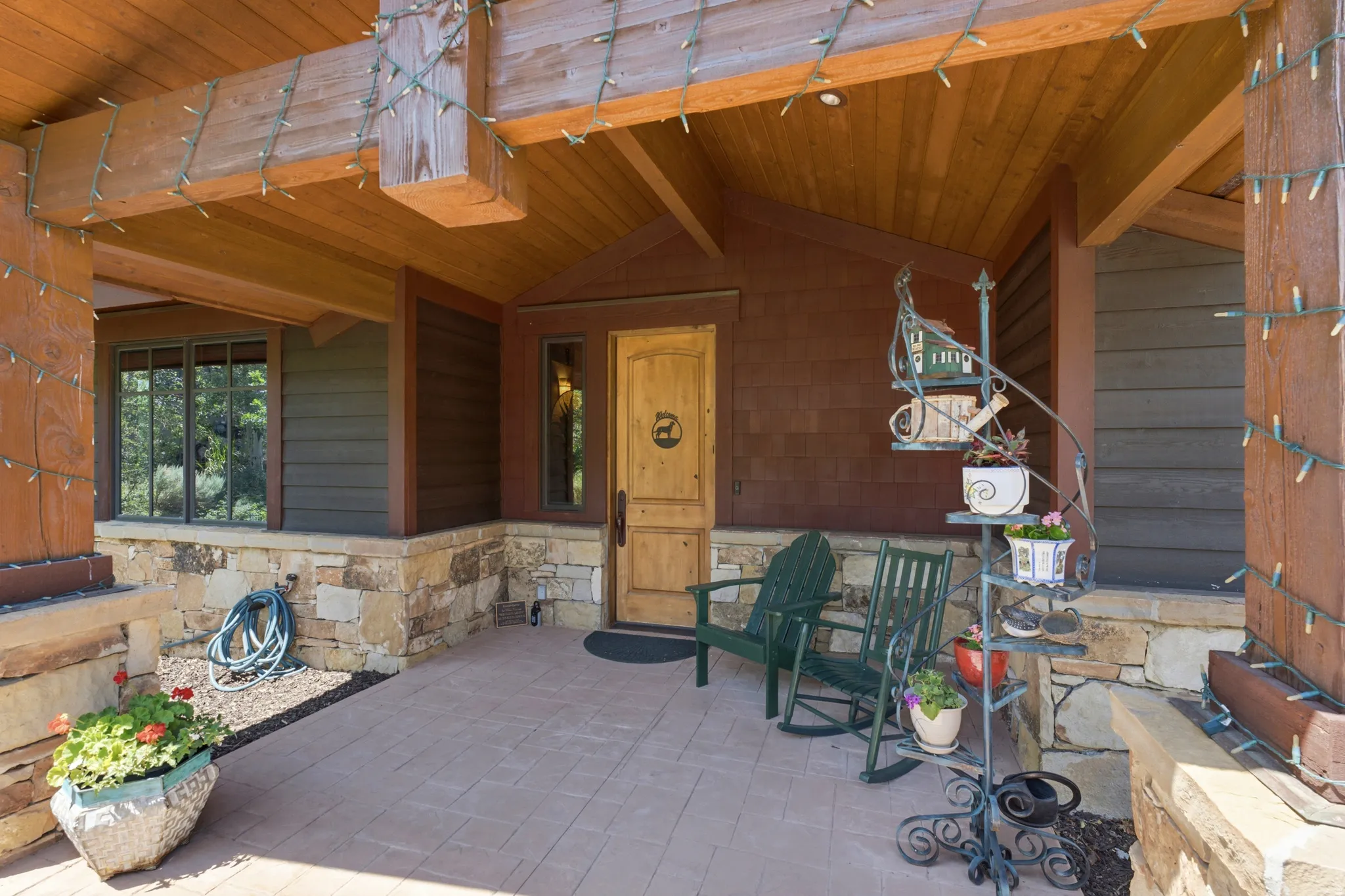 Covered front porch featuring a wood-finish ceiling, exposed wood beams, and a natural stone-clad foundation