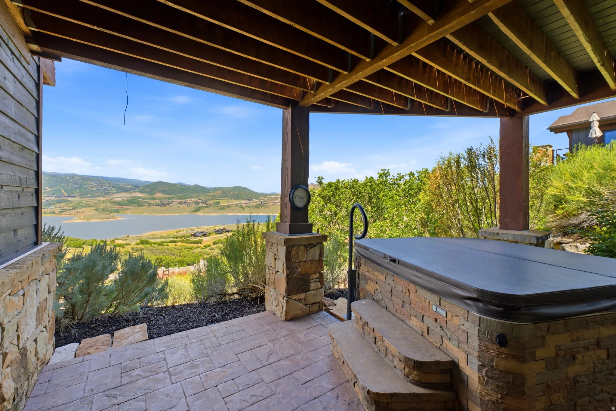 Covered patio featuring a built-in spa with stone surround, stamped concrete flooring, and distant lake scenery