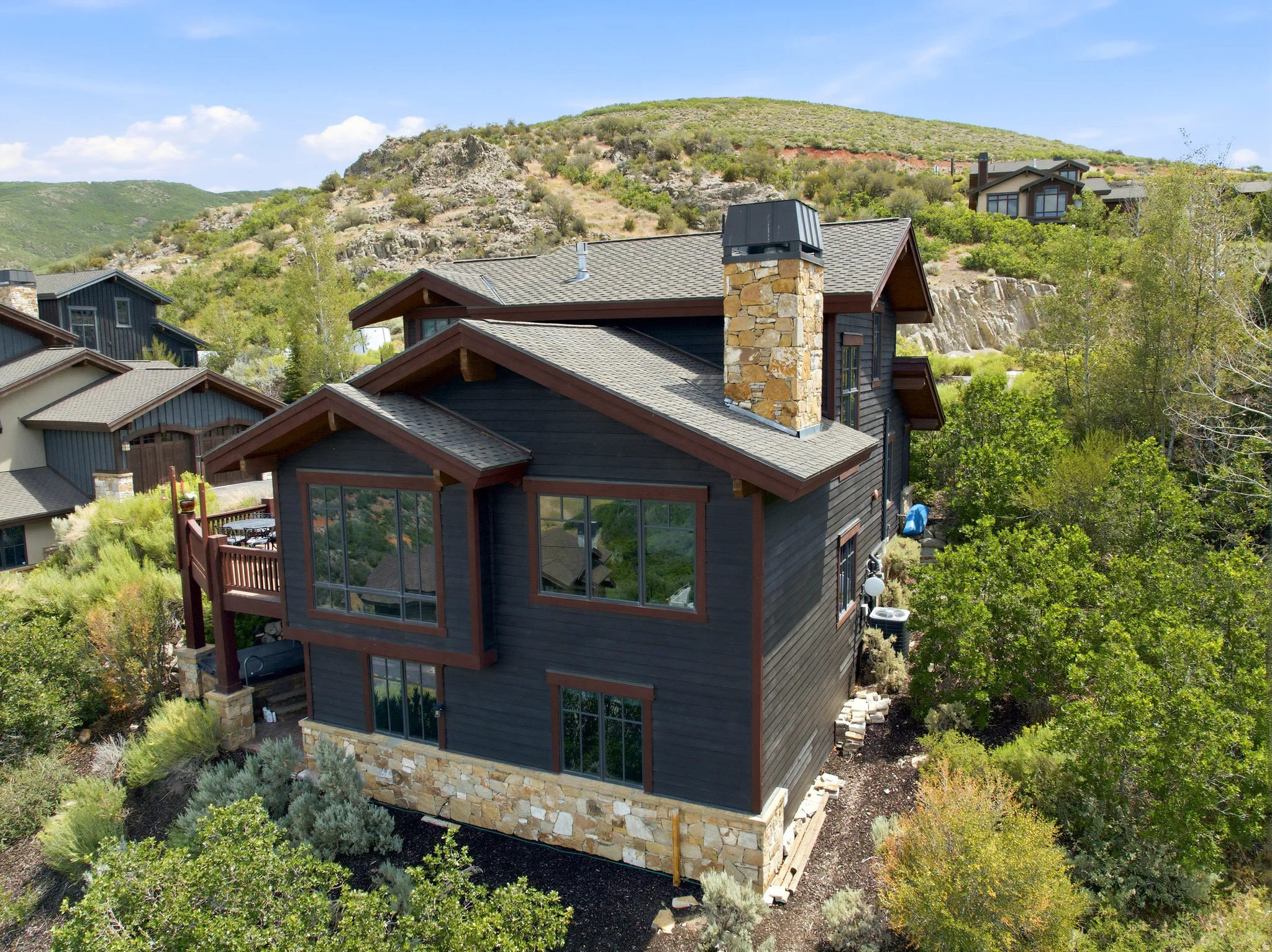 Multi-level residence featuring dark siding, stone accents, and an elevated wooden deck