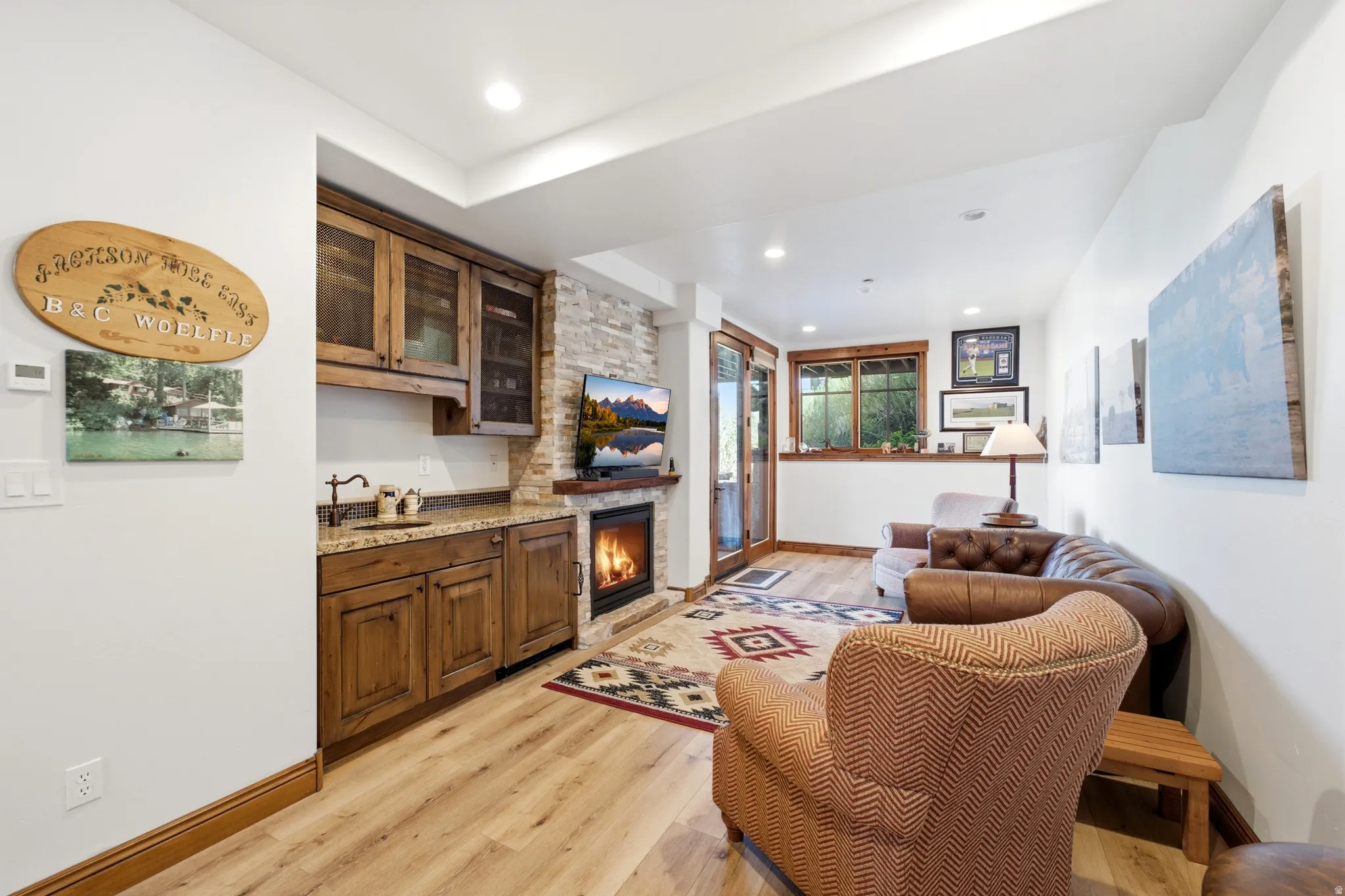 Recessed lighting illuminates wood-finish flooring in this living space, featuring a stone-clad fireplace with a wood mantel