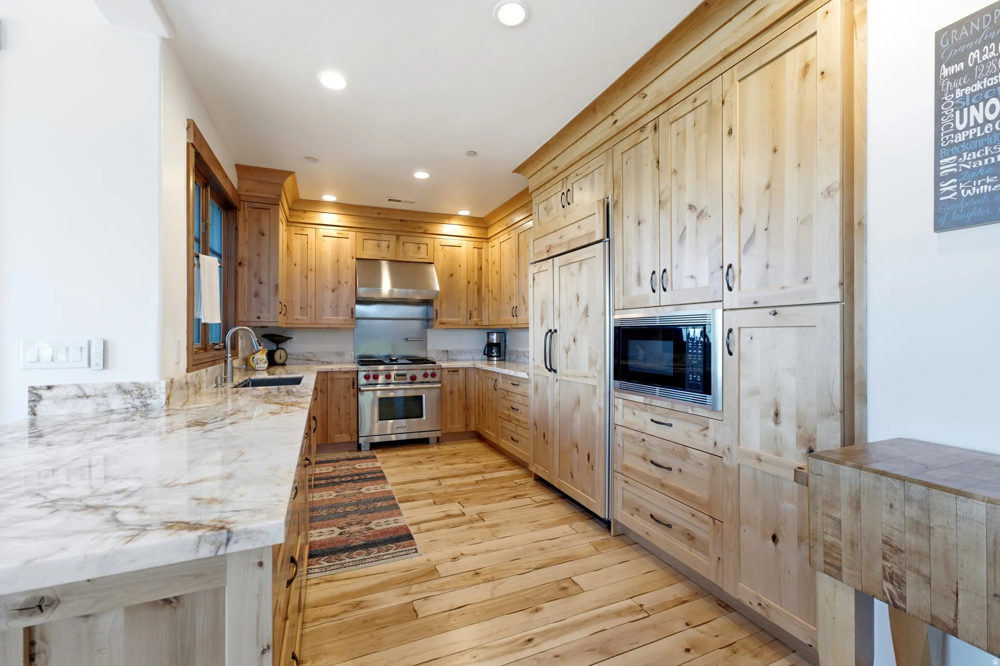 Kitchen featuring extensive wood cabinetry, wood-finish flooring, stone countertops, stainless steel appliances, and recessed lighting