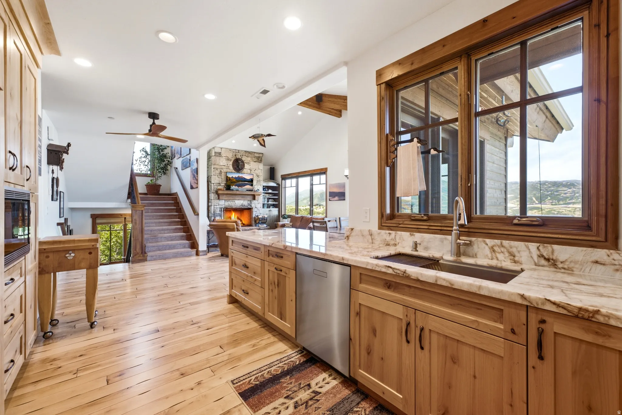 Kitchen featuring wood-finish cabinetry, light-toned stone countertops, and a stainless steel undermount sink with a gooseneck faucet