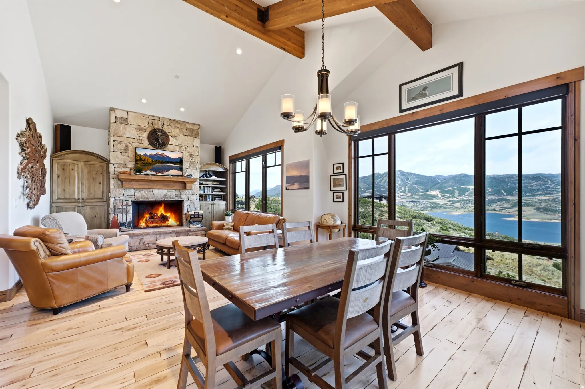 Vaulted ceiling great room with exposed wood beams, a stone fireplace, and wide-plank wood-finish flooring