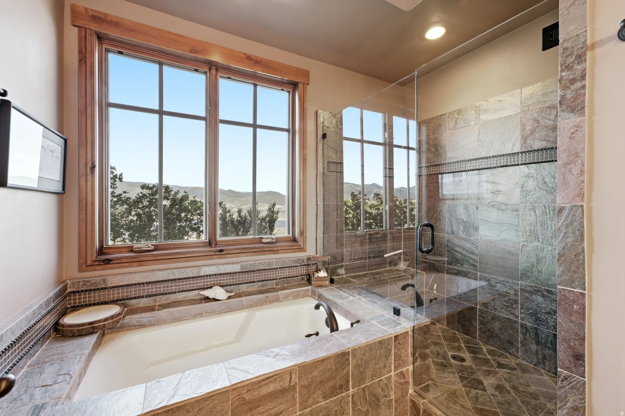 Soaking tub with a wood-trimmed window, tiled surround, and integrated mosaic tile accent