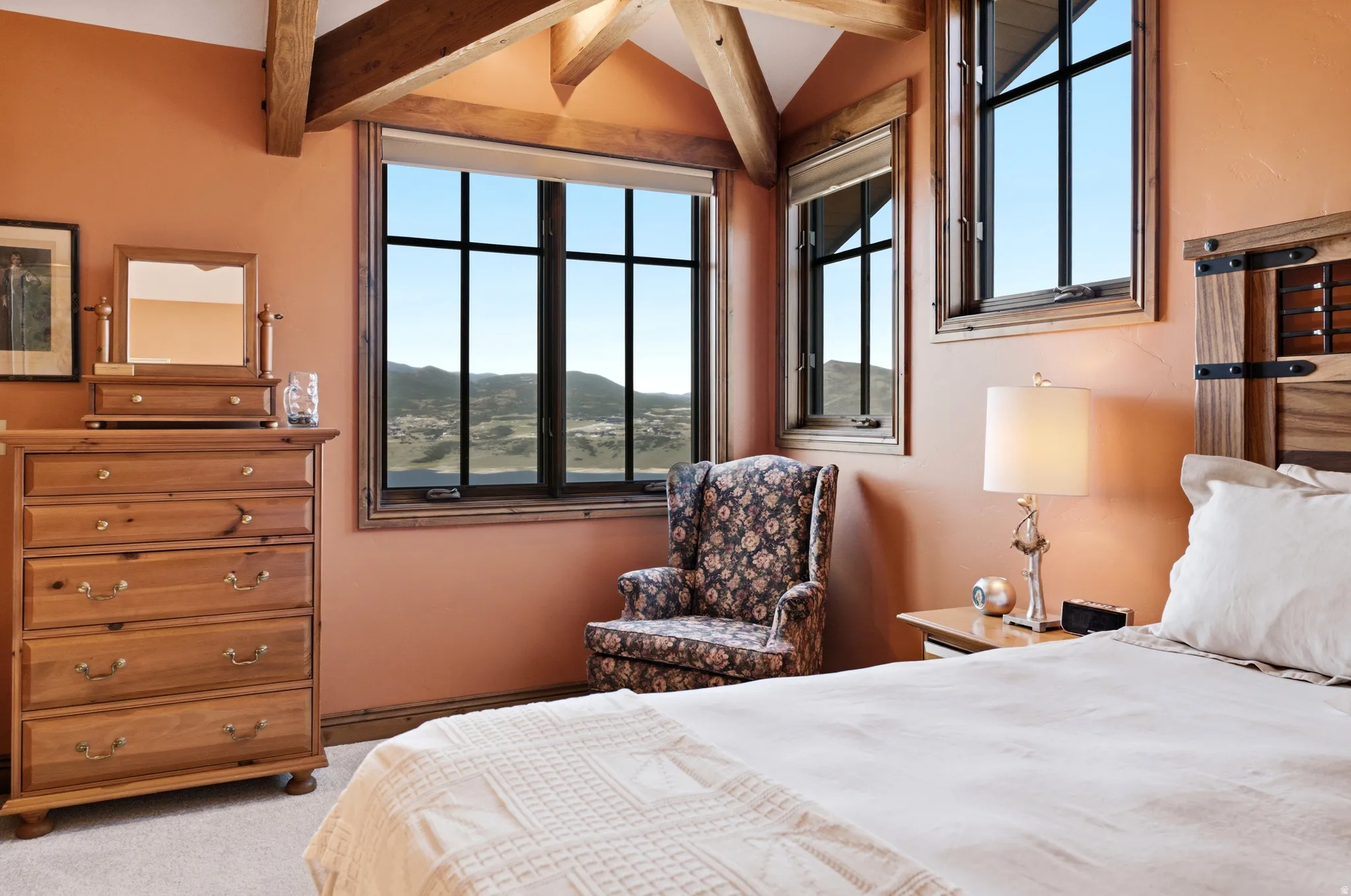 Bedroom featuring exposed wood ceiling beams, multiple grid-pattern windows, light coral wall finish, and wood trim details