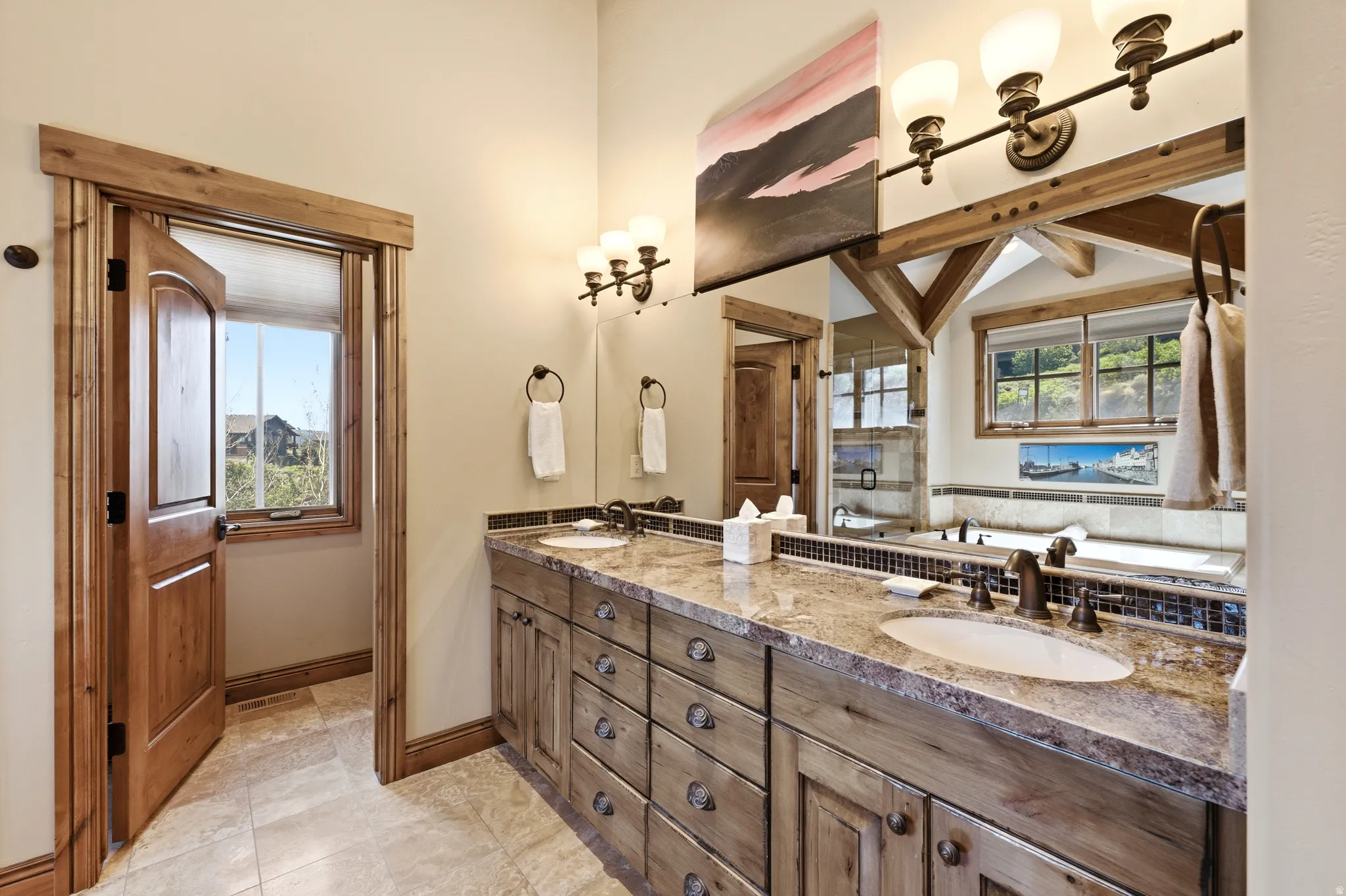 Double vanity featuring granite countertops, undermount sinks, and rustic wood cabinetry with decorative hardware