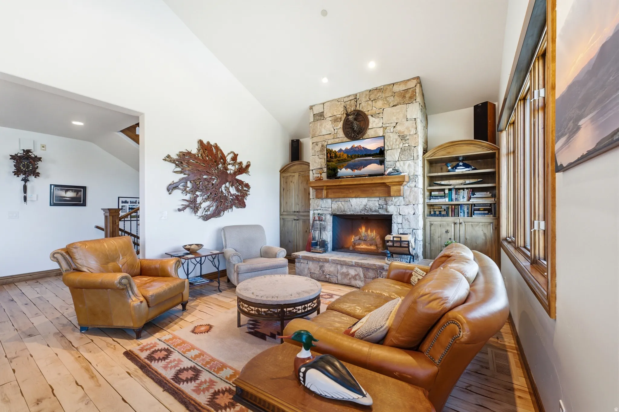 Living area featuring a stone-clad fireplace with a wood mantel, vaulted ceiling, and wide plank wood-finish flooring