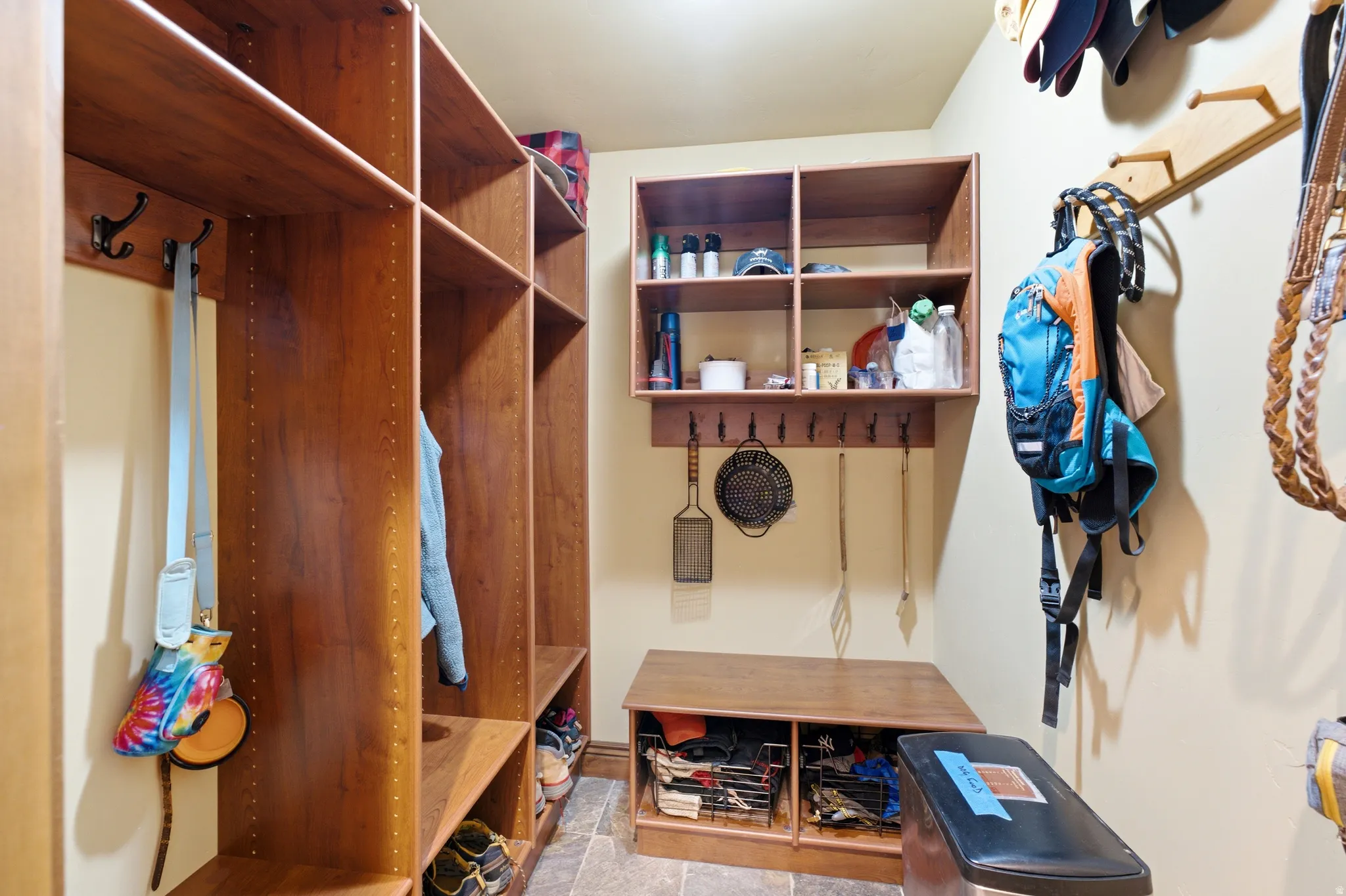 Mudroom featuring extensive wood-finish cabinetry, integrated storage cubbies, built-in bench seating, multiple coat hooks, and stone tile flooring