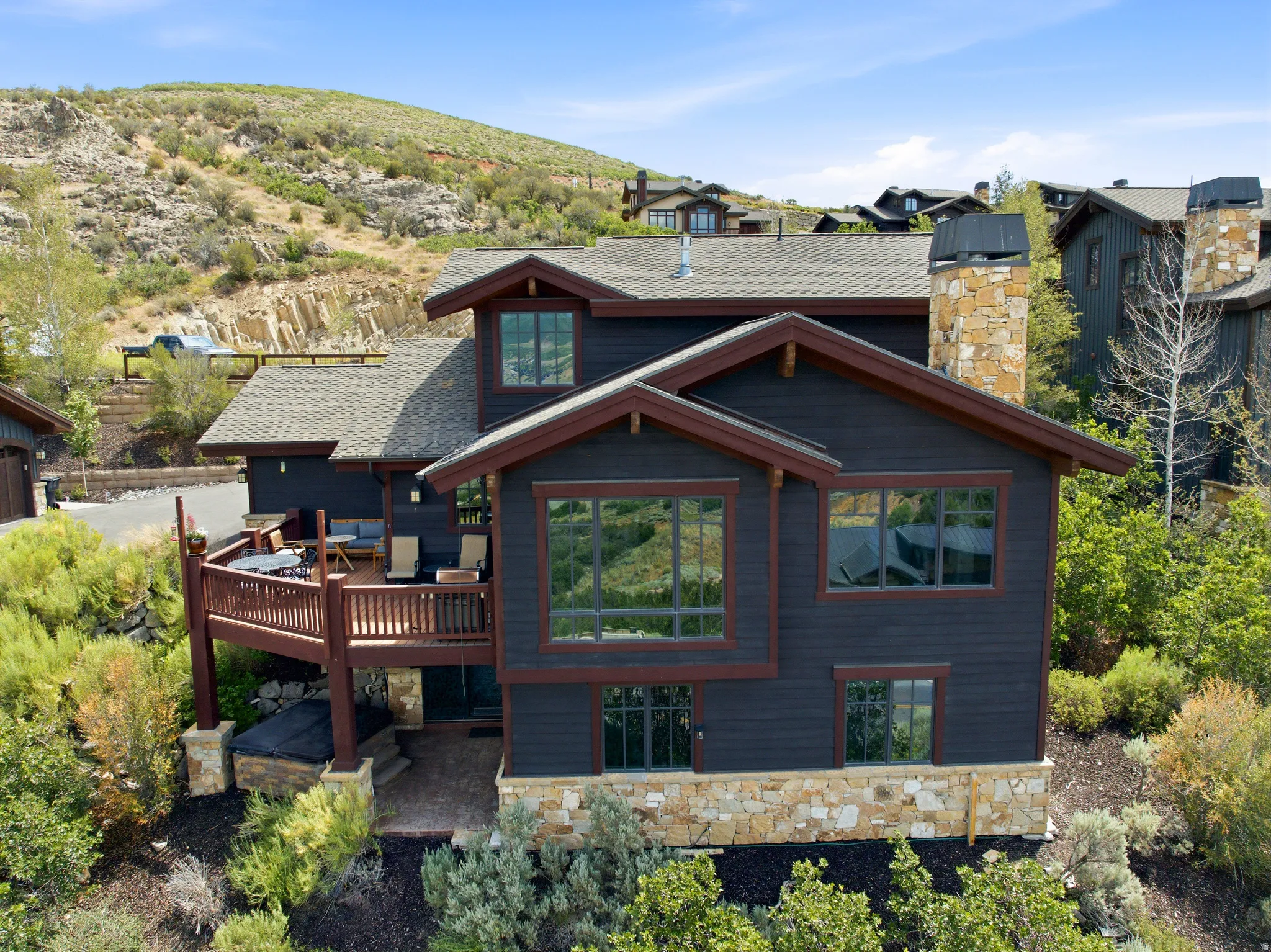 Multi-level residence featuring dark siding, stone accents, and a prominent deck