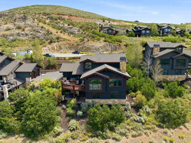 Modern mountain architecture featuring a dark exterior, stone accents, multiple large windows, a spacious wood deck, and a stone chimney