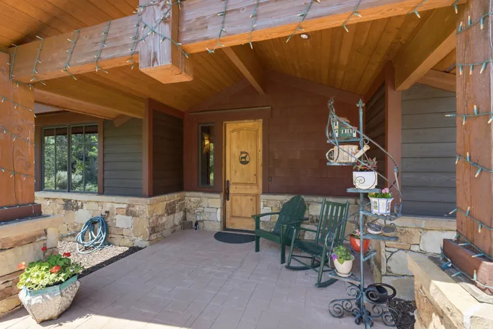 Covered front porch featuring a wood-finish ceiling, exposed wood beams, and a natural stone-clad foundation