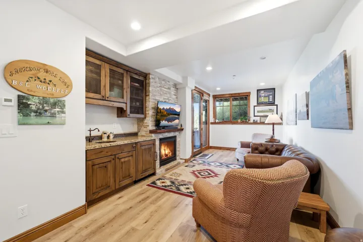 Recessed lighting illuminates wood-finish flooring in this living space, featuring a stone-clad fireplace with a wood mantel