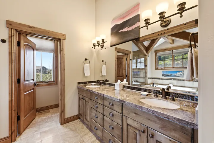 Double vanity featuring granite countertops, undermount sinks, and rustic wood cabinetry with decorative hardware