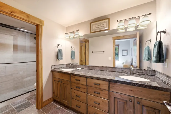 Guest Room Ensuite Double vanity featuring wood cabinetry, undermount sinks, and granite countertops with a mosaic tile backsplash