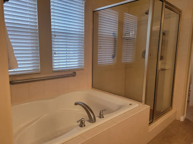Enclosed glass shower stall with a built-in tub featuring brushed nickel fixtures