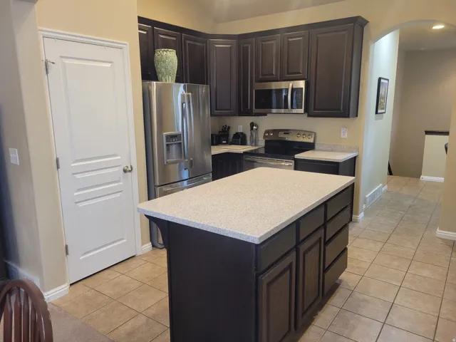 Kitchen featuring dark wood cabinetry, stainless steel appliances, a center island with countertop, and tile flooring