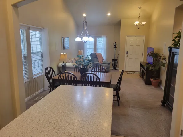 Open-concept living area featuring a dining space with a wood-finish table, carpet flooring, multiple windows with blinds, and recessed lighting