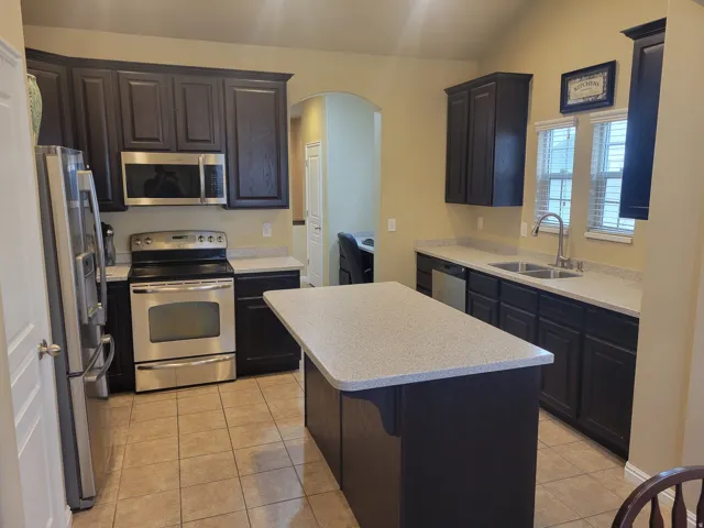 Kitchen featuring dark wood cabinetry, light speckled countertops, stainless steel appliances, a center island, and tile flooring