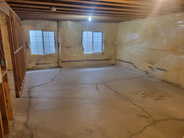 Unfinished basement with exposed wood joists, concrete flooring, two windows, and insulated walls