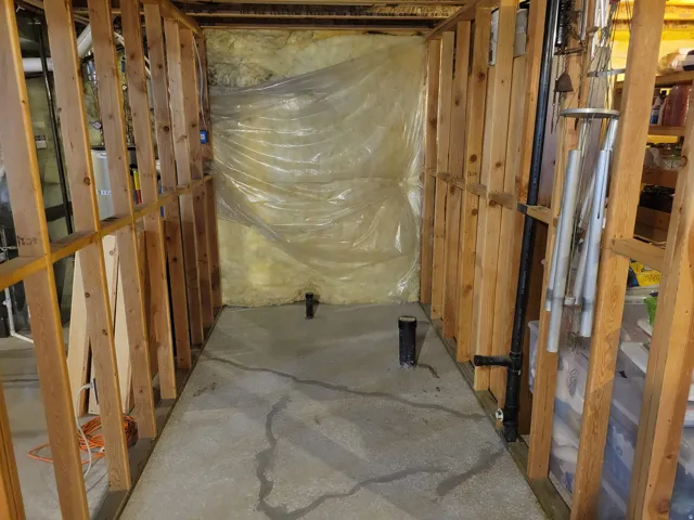 Basement area framed for future development, featuring concrete flooring, exposed insulation, plumbing rough-ins, and a vapor barrier