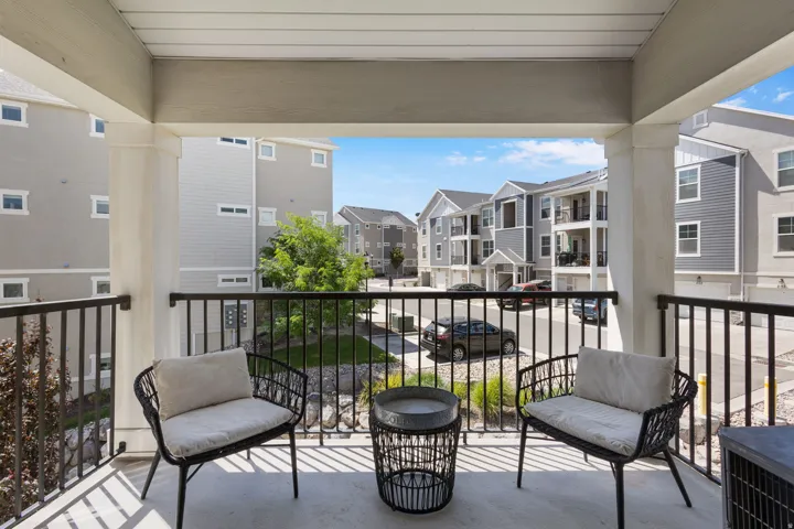 Covered outdoor balcony with concrete flooring, black metal railings, and two substantial pillars