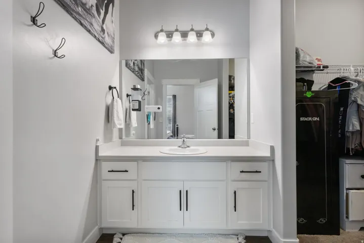 White vanity cabinet with a single basin sink and a light-colored countertop