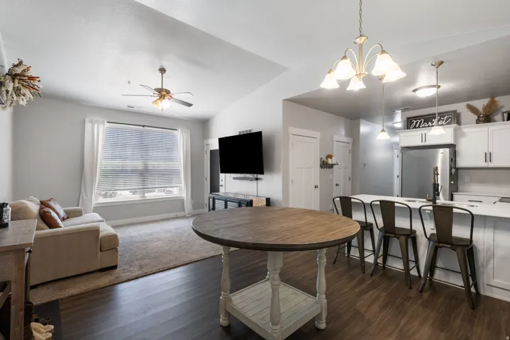 Open-concept living space featuring vaulted ceilings, wood-finish flooring, a kitchen island with seating, white cabinetry, and stainless steel appliances