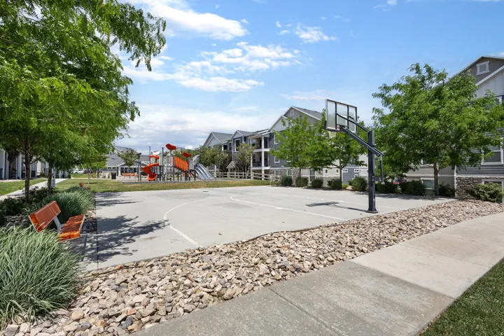 Outdoor basketball court with a playground, green space, and mature trees