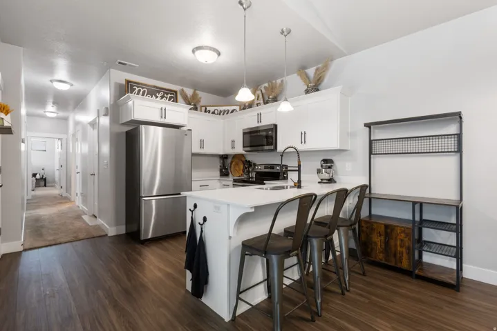 Modern kitchen featuring white cabinetry, a central island with countertop seating, stainless steel appliances, dark wood-finish flooring, and pendant lighting