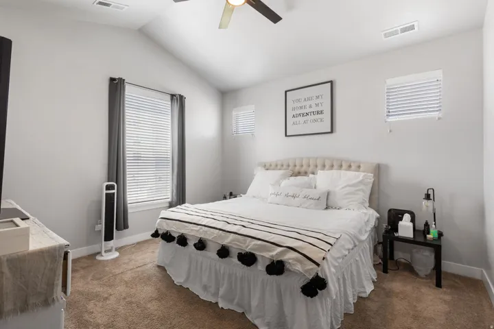 Vaulted ceiling with a ceiling fan, multiple windows with blinds, light-colored walls, and carpeting