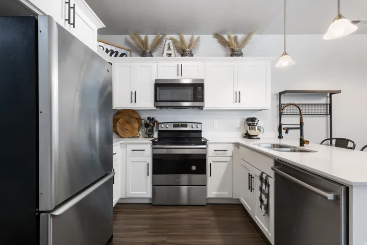 Modern kitchen featuring white cabinetry, stainless steel appliances, light-toned countertops, wood-finish flooring, and pendant lighting