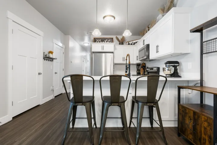 Kitchen featuring white cabinetry, stainless steel refrigerator, dark wood-finish flooring, and a breakfast bar with seating