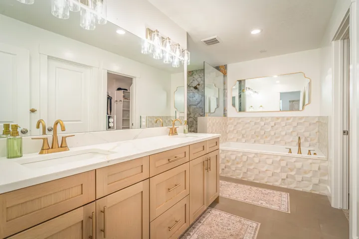 Dual vanity with light wood-finish cabinetry, white countertops, and gold-finish fixtures