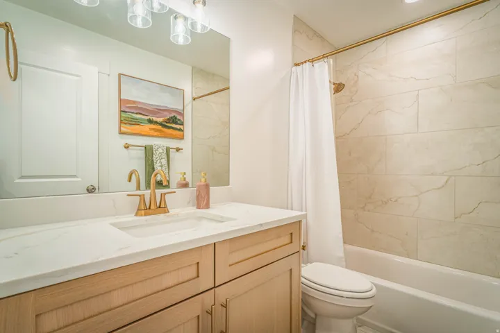 Bathroom featuring a wood-finish vanity with a white countertop, an undermount sink, and a gold-finish faucet